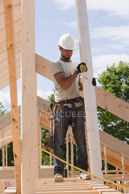 Carpintero sosteniendo una viga de techo en el sitio de construcción del edificio - foto de stock