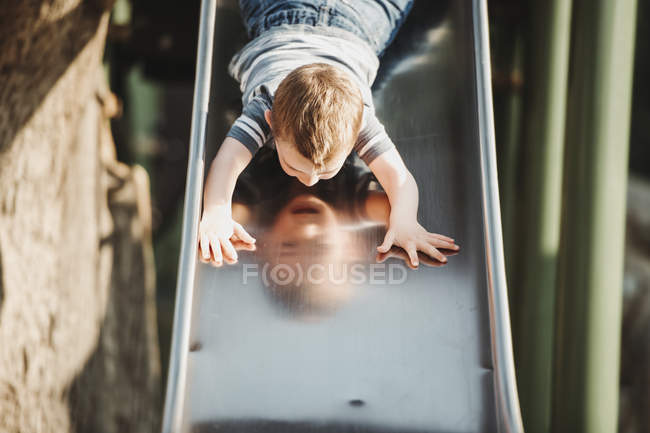 Giovane ragazzo che scende a testa in giù su uno scivolo parco giochi; Edmonton, Alberta, Canada — Foto stock