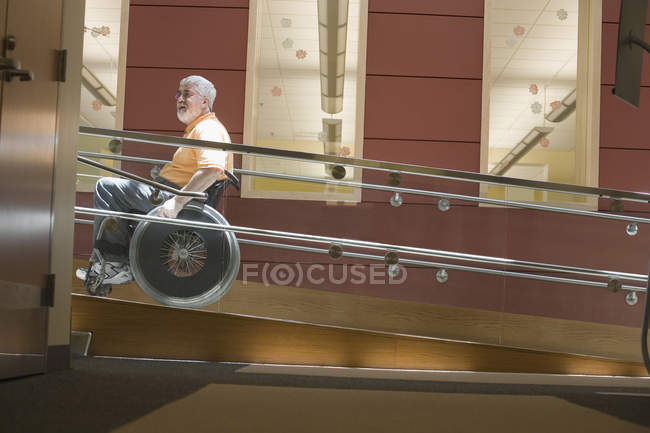 Profil latéral d'un homme mature atteint de dystrophie musculaire assis dans un fauteuil roulant sur une rampe d'accès pour fauteuil roulant — Photo de stock