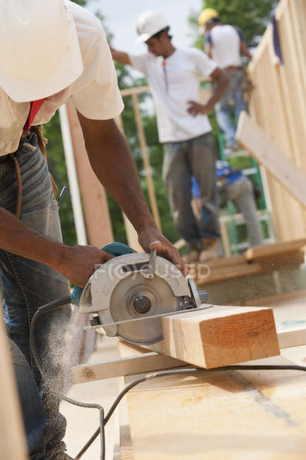 Carpenter cutting a joist with a circular saw at building construction site — Stock Photo