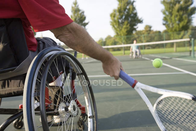 Vista de sección baja de un hombre sentado en una silla de ruedas y jugando al tenis . - foto de stock