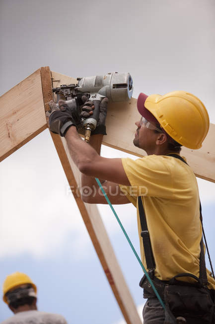 Carpinteiro pregar telhado vigas com uma pistola de prego — Fotografia de Stock