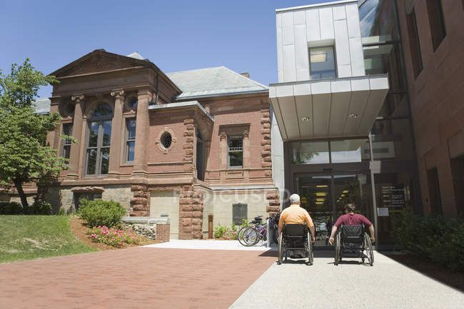 Visão traseira de duas pessoas com distrofia muscular em frente a um prédio da biblioteca — Fotografia de Stock