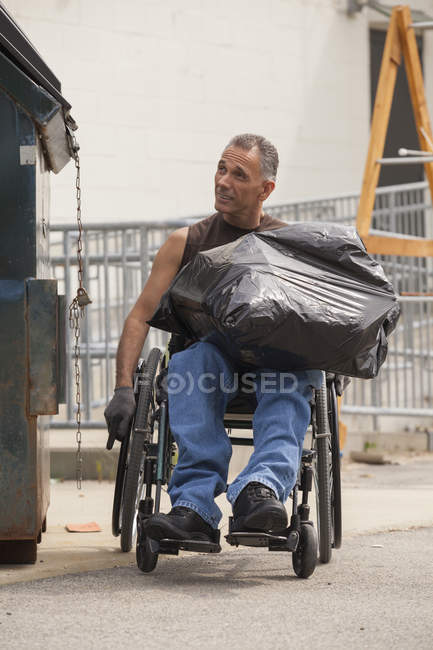 Carregando o trabalhador portuário com lesão medular em uma cadeira de rodas colocando um saco no lixo — Fotografia de Stock