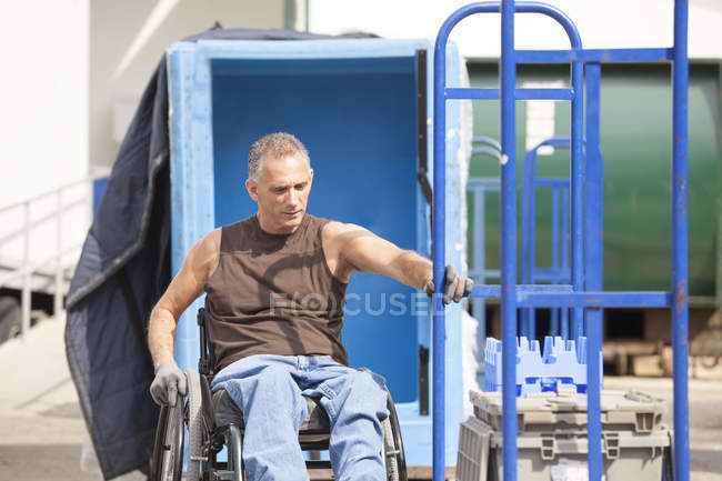 Carregando o trabalhador portuário com lesão medular em uma cadeira de rodas movendo um caminhão de mão — Fotografia de Stock