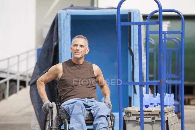 Trabajador portuario de carga con lesión medular en silla de ruedas en zona de almacenamiento - foto de stock