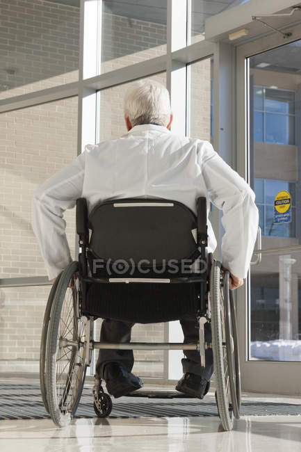 Doctor with muscular dystrophy in wheelchair at hospital entrance — Stock Photo