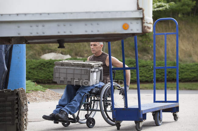 Chargement docker avec lésion de la moelle épinière dans un fauteuil roulant mobiles plateaux d'inventaire empilés — Photo de stock