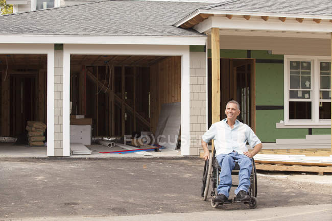 Man with spinal cord injury in a wheelchair at his new accessible home under construction — Stock Photo