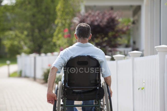 Homem com lesão medular em uma cadeira de rodas em um passeio subúrbio com casas — Fotografia de Stock