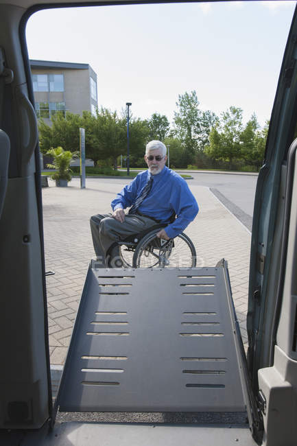 Человек с мышечной дистрофией и диабетом в инвалидной коляске, смотрящий с ворот доступного фургона — стоковое фото
