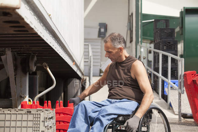 Chargement docker avec lésion de la moelle épinière dans un fauteuil roulant empilant plateaux d'inventaire — Photo de stock
