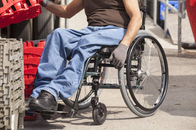 Loading dock worker with spinal cord injury in a wheelchair stacking inventory trays — Stock Photo