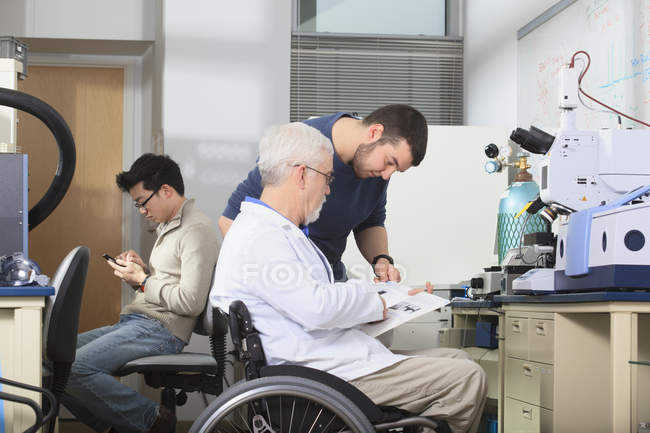 Professor with muscular dystrophy working with students in a laboratory — Stock Photo