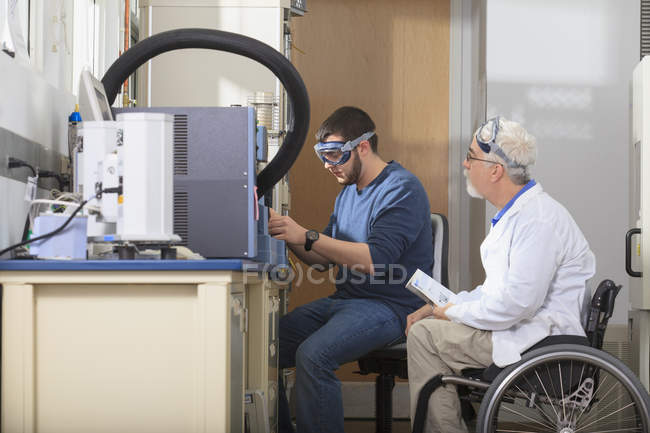 Professeur avec dystrophie musculaire travaillant avec des étudiants dans un laboratoire — Photo de stock