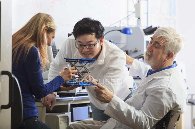 Profesor con distrofia muscular trabajando con estudiantes en un laboratorio - foto de stock