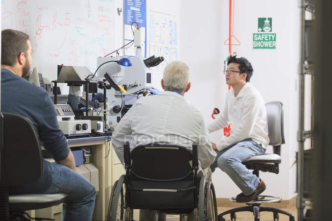 Профессор с мышечной дистрофией работает со студентами в лаборатории — стоковое фото