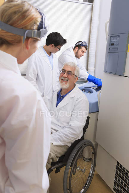 Profesor con distrofia muscular trabajando con estudiantes en un laboratorio - foto de stock