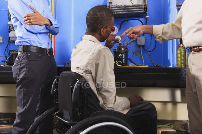 Ausbilder diskutiert mit Schüler im Rollstuhl über Kondensatorspule an Kühlgerät — Stockfoto