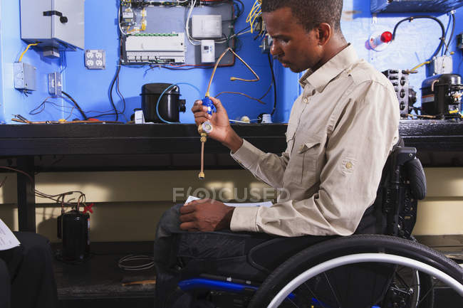 Student in wheelchair examining air conditioner high pressure line in HVAC classroom — Stock Photo