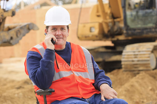 Construction engineer with spinal cord injury on radio to equipment operator — Stock Photo