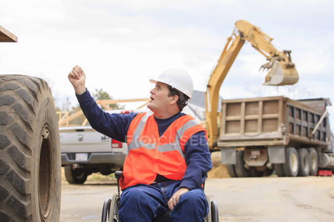 Construction engineer with spinal cord injury talking with front end loader operator — Stock Photo