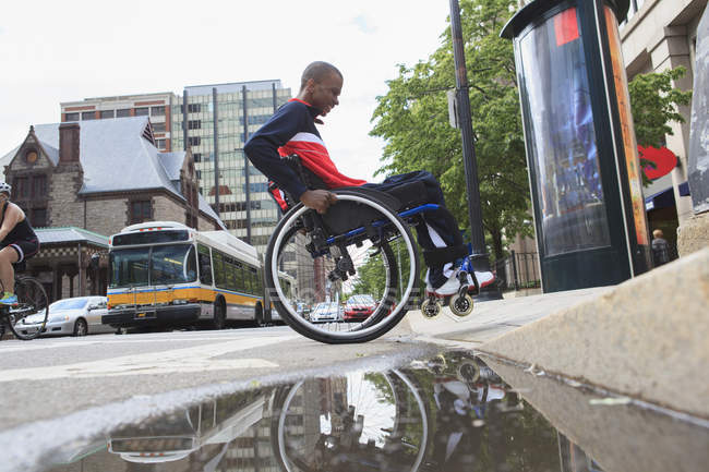 Homem em cadeira de rodas que tinha meningite espinhal passando por um meio-fio — Fotografia de Stock