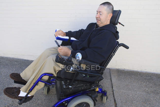 Uomo con lesione del midollo spinale e braccio con danni ai nervi in sedia a rotelle motorizzata guardando smart phone — Foto stock