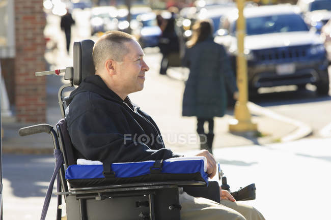 Человек с травмой спинного мозга и руки с повреждением нерва в моторизованной инвалидной коляске, переходящей улицу — стоковое фото