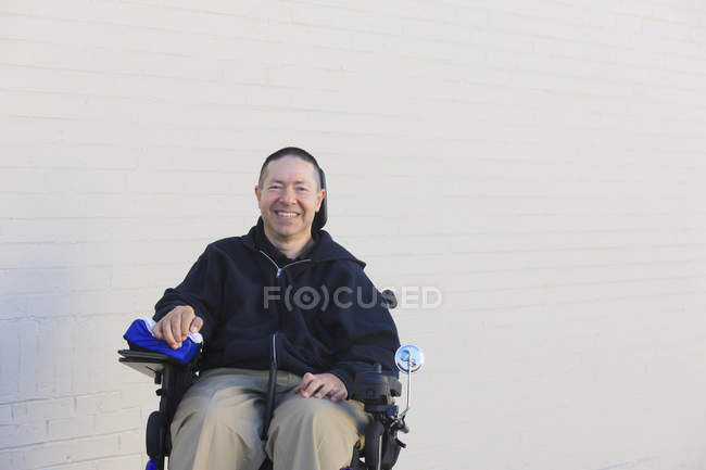 Hombre con lesión medular y brazo con daño nervioso en silla de ruedas motorizada - foto de stock