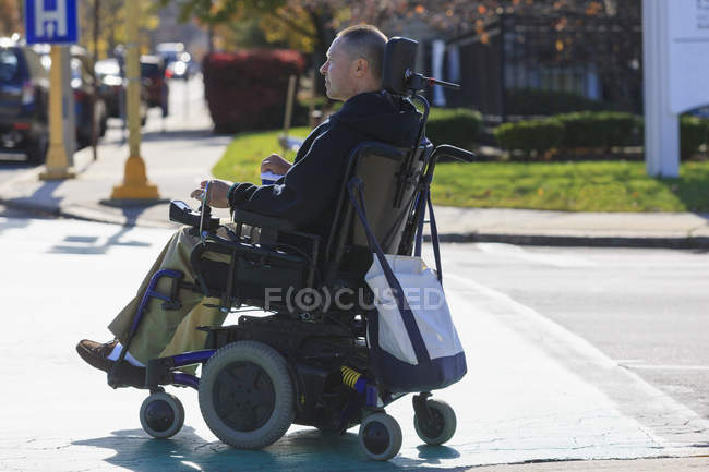 Человек с травмой спинного мозга и руки с повреждением нерва в моторизованной инвалидной коляске, переходящей улицу — стоковое фото