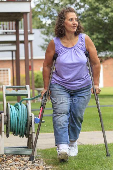 Frau mit Spina bifida geht mit Krücken und zieht Gartenschlauch — Stockfoto