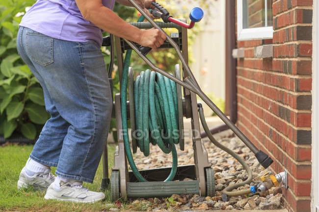 Frau mit Spina bifida mit Krücken und Gartenschlauch ziehen — Stockfoto