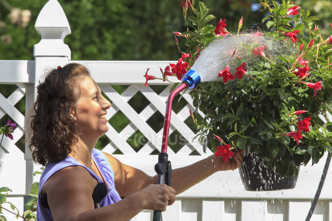 Frau mit Spina bifida versprüht Blumen mit Gartenschlauch — Stockfoto