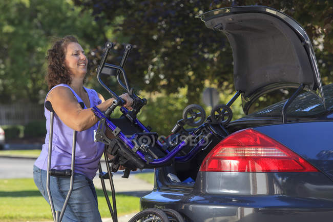 Женщина со Спиной Бифидой сажает инвалидное кресло на заднее сиденье машины — стоковое фото