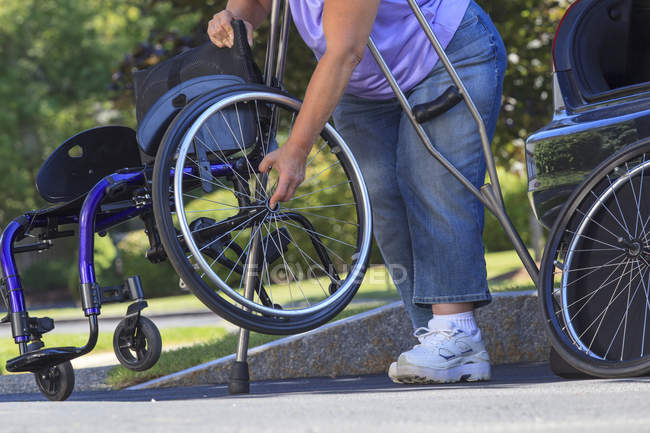 Mulher com Spina Bifida usando muletas para montar uma cadeira de rodas depois de viajar no carro — Fotografia de Stock