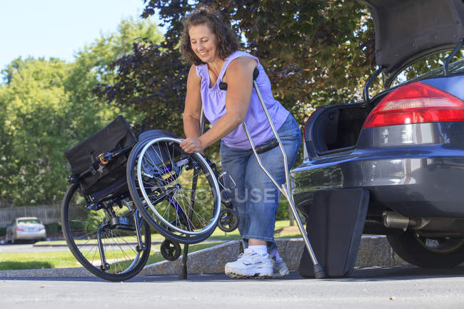 Mulher com Spina Bifida usando muletas para desmontar a cadeira de rodas para viajar no carro — Fotografia de Stock