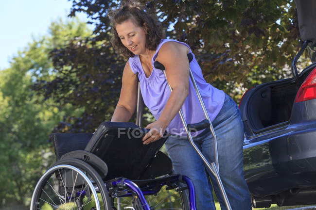 Donna con Spina Bifida usando le stampelle per smontare la sedia a rotelle per viaggiare in auto — Foto stock