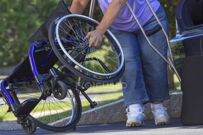 Mujer con Espina Bifida usando muletas para desmontar silla de ruedas para viajar en el coche - foto de stock
