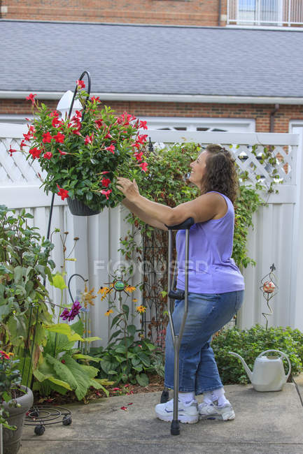 Femme avec Spina Bifida sur des béquilles fixant des fleurs en été — Photo de stock