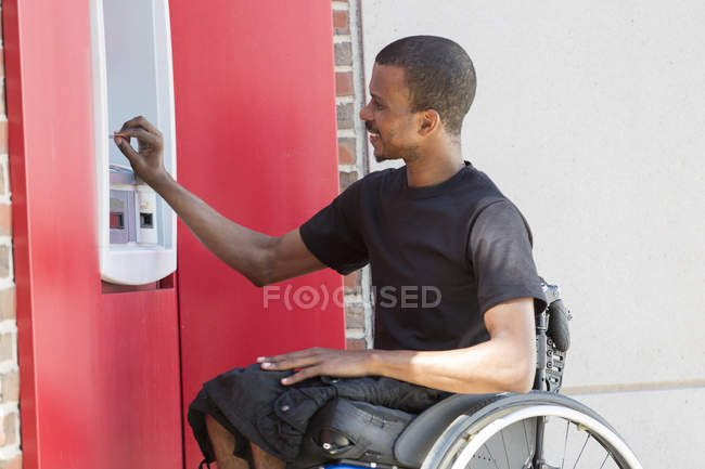 Чоловік, який переніс спінальний менінгіт у інвалідному візку на банківському атомі. — стокове фото