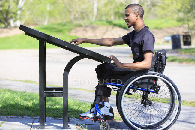 Homme souffrant de méningite rachidienne en fauteuil roulant lisant un répertoire du parc — Photo de stock