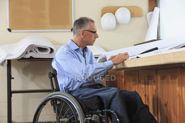 Ingeniero de proyecto con una lesión en la médula espinal en una silla de ruedas mirando dibujos - foto de stock