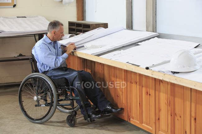 Project engineer with a Spinal Cord Injury in a wheelchair using a tablet to study drawings — Stock Photo
