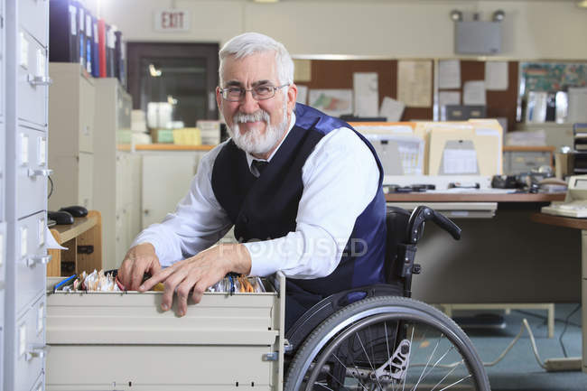 Uomo con distrofia muscolare in sedia a rotelle che lavora in un ufficio — Foto stock