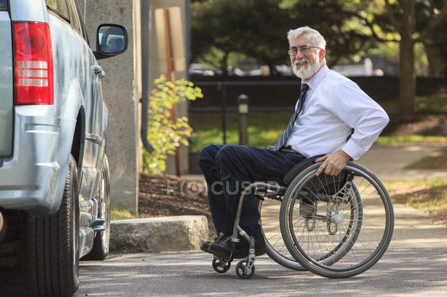 Hombre con distrofia muscular en silla de ruedas que entra en su furgoneta accesible en el estacionamiento de la oficina - foto de stock