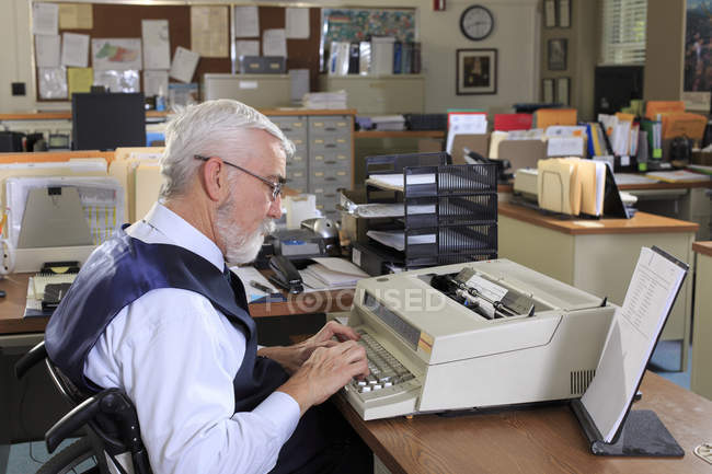 Человек с мышечной дистрофией в инвалидном кресле работает в офисе — стоковое фото