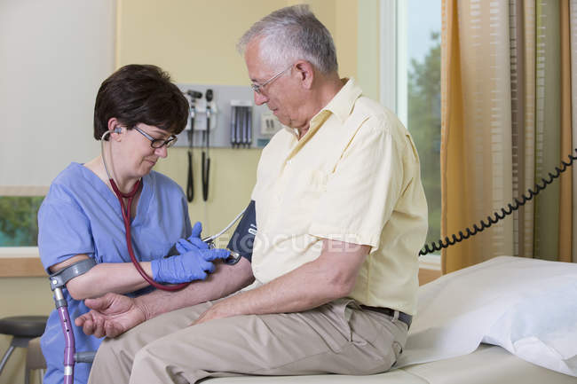 Krankenschwester mit Zerebralparese am Stock bei der Blutdruckkontrolle eines Patienten — Stockfoto