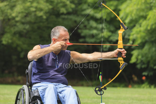 Man with spinal cord injury in wheelchair aiming his bow and arrow for archery practice — Stock Photo