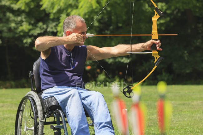 Людина з травмою спинного мозку в інвалідному візку націлена на його лук і стрілу для тренування з стрільби з лука — стокове фото
